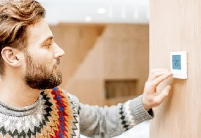 man adjusting heating thermostat on wall